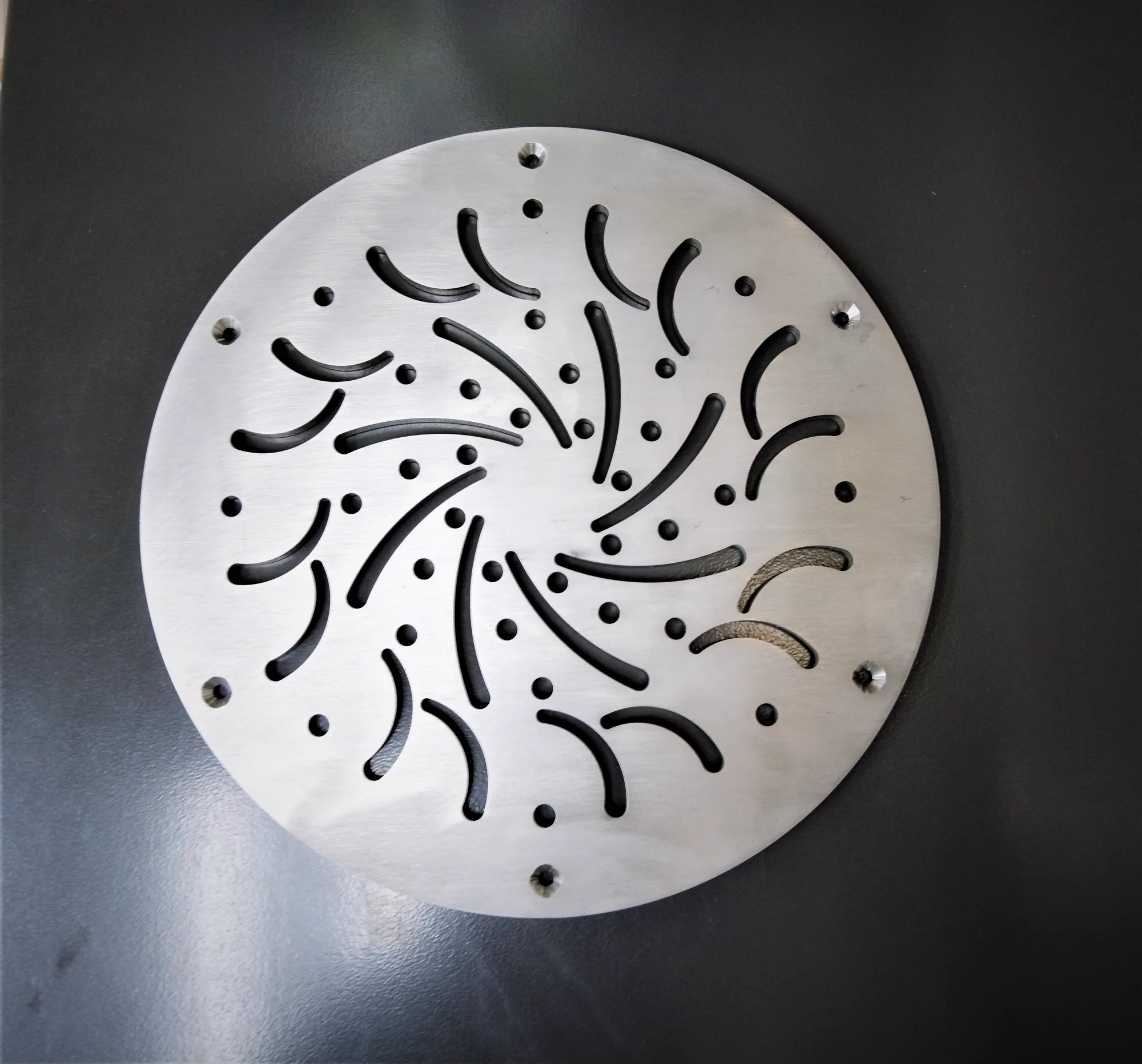 Finished precision-cut circular metal sample with clean curved slots and countersunk holes
